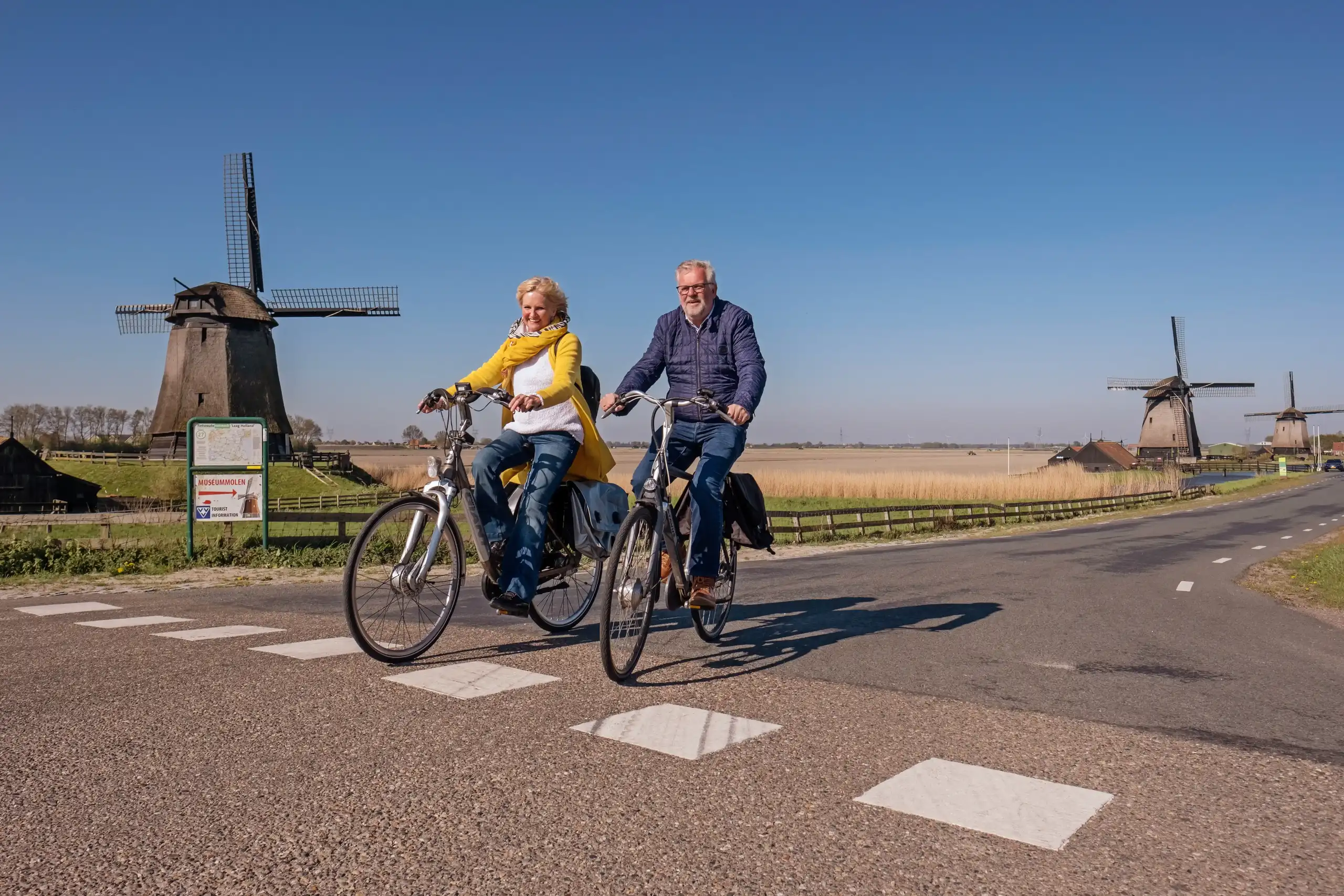 Man en vrouw op de fiets met molens op de achtergrond